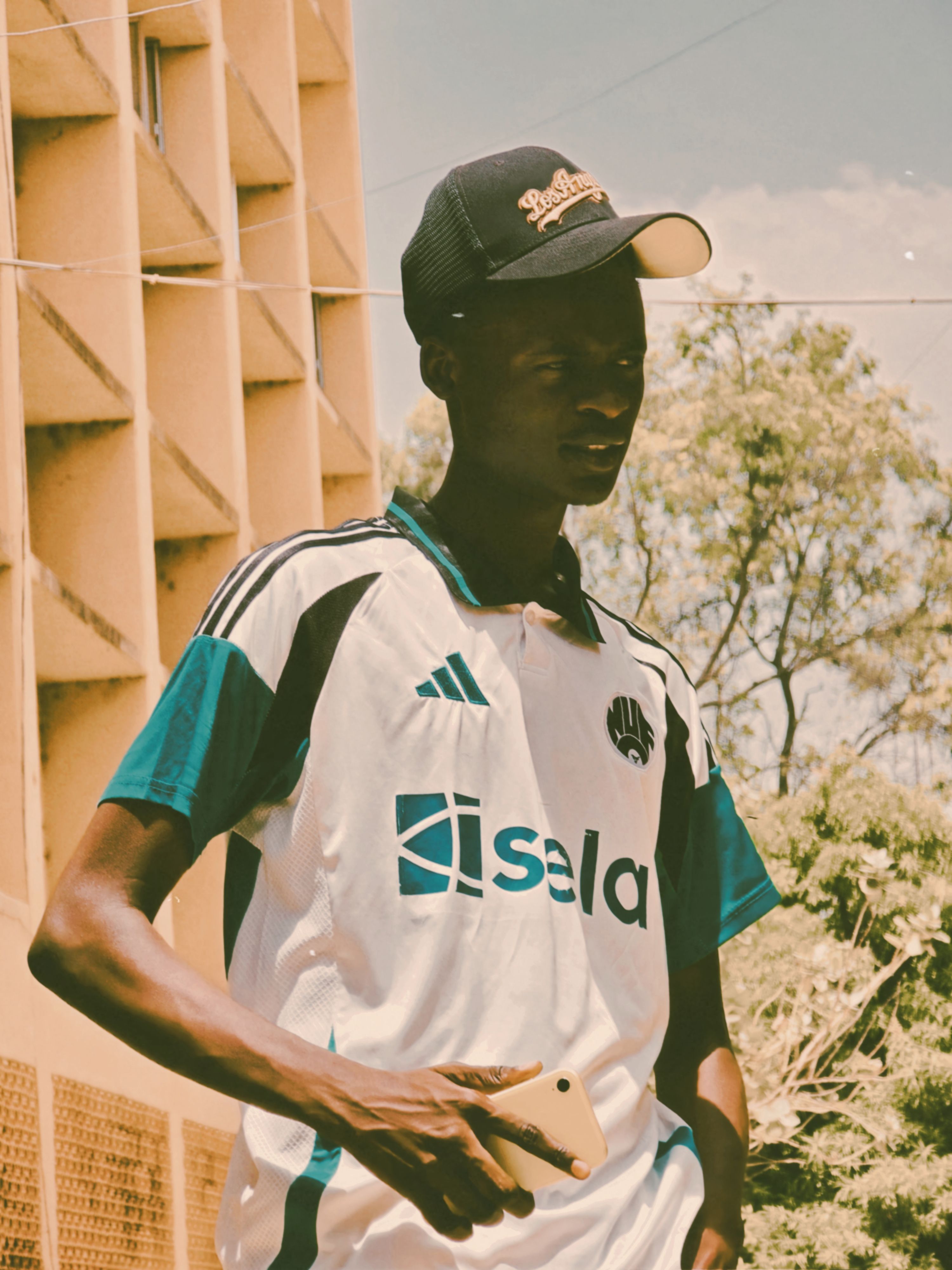 Young man in cap and sports jersey holding smartphone outdoors.