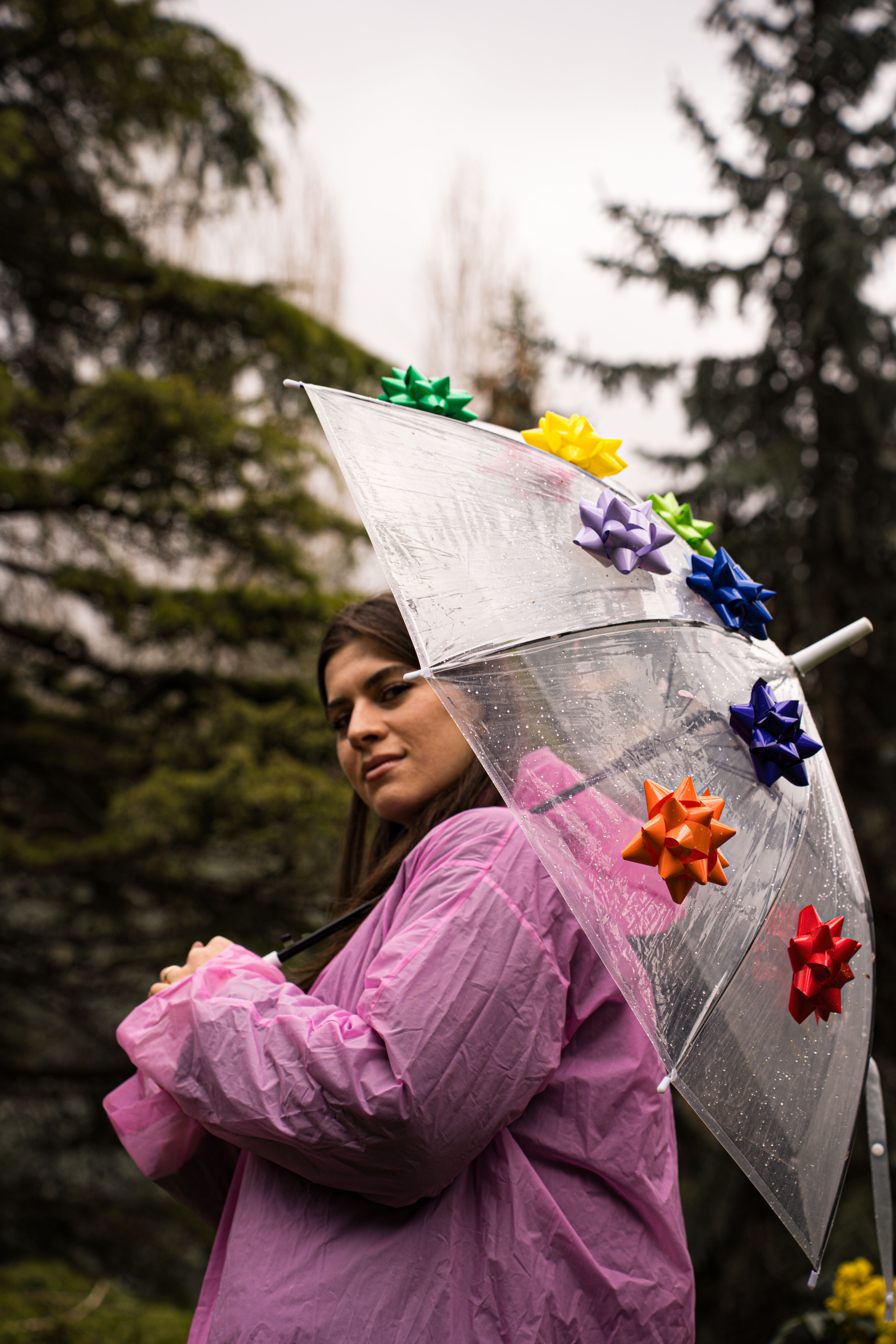 A woman wearing a pink coat holds an umbrella with colorful bows on a rainy day.