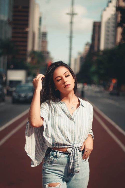 Free Stylish woman in casual wear posing on a vibrant city street with closed eyes. Stock Photo
