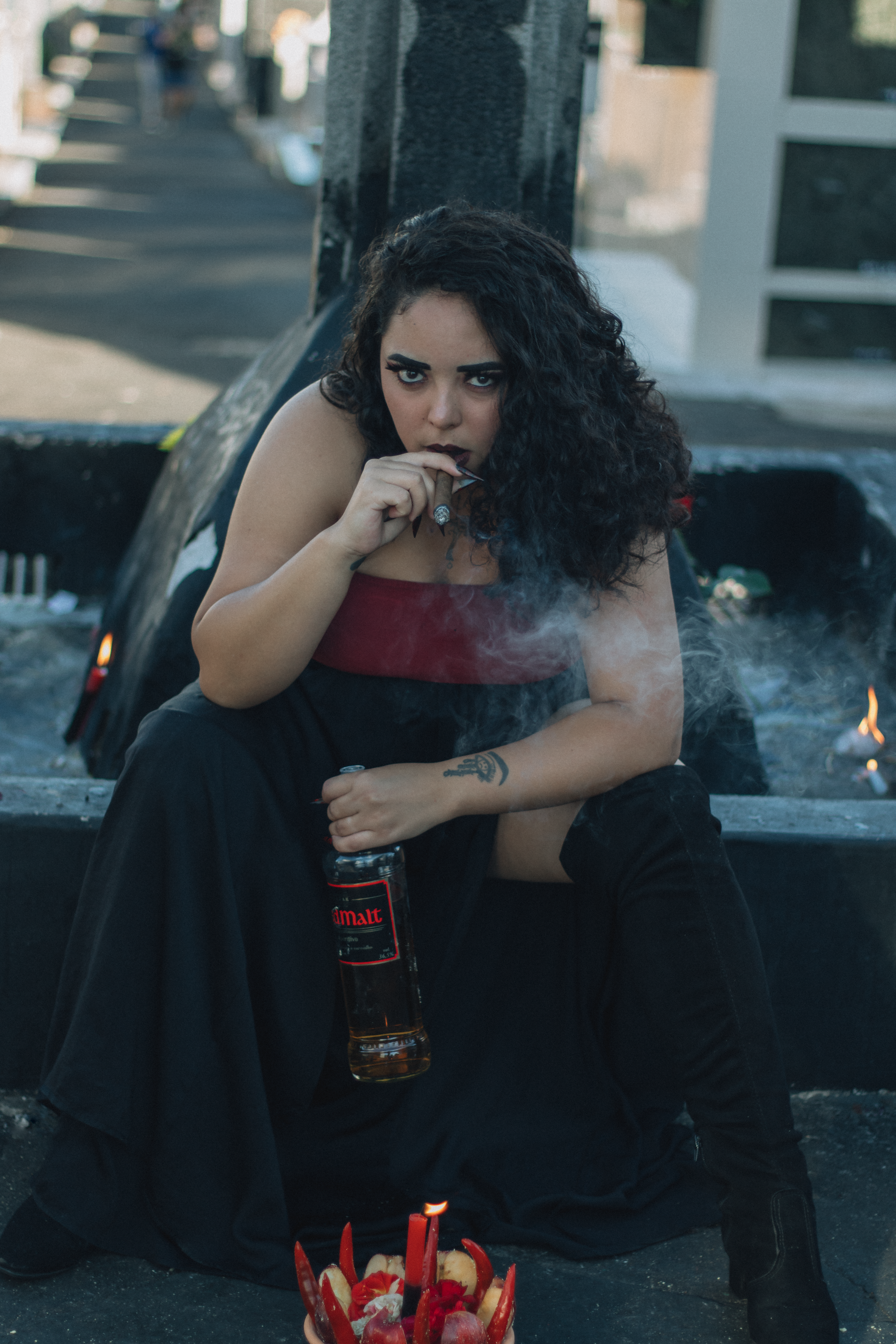 Woman smoking and holding a bottle outdoors with graffiti backdrop.