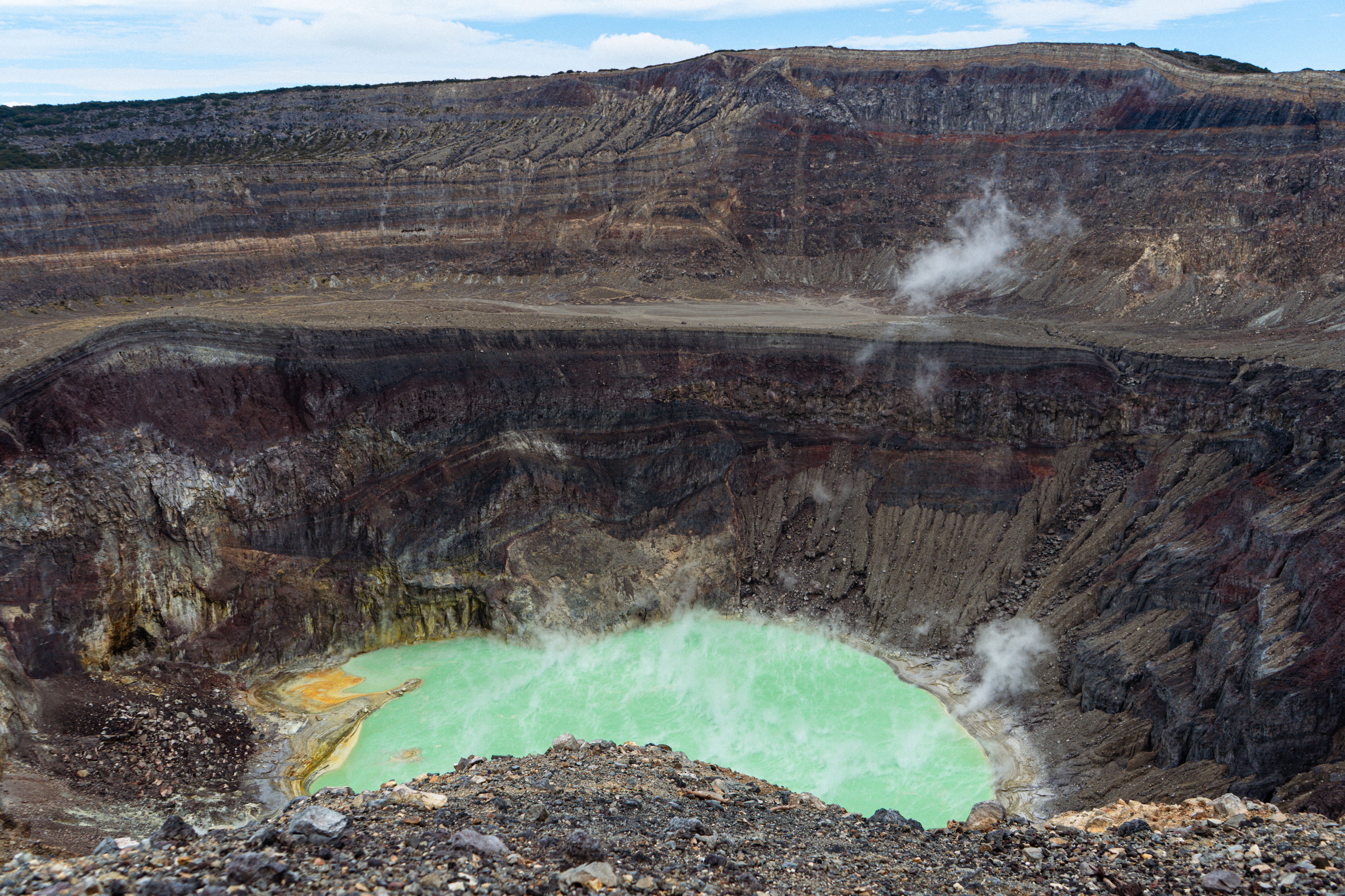A breathtaking view of an active volcano crater with a vibrant sulfuric lake emitting steam under a clear sky.