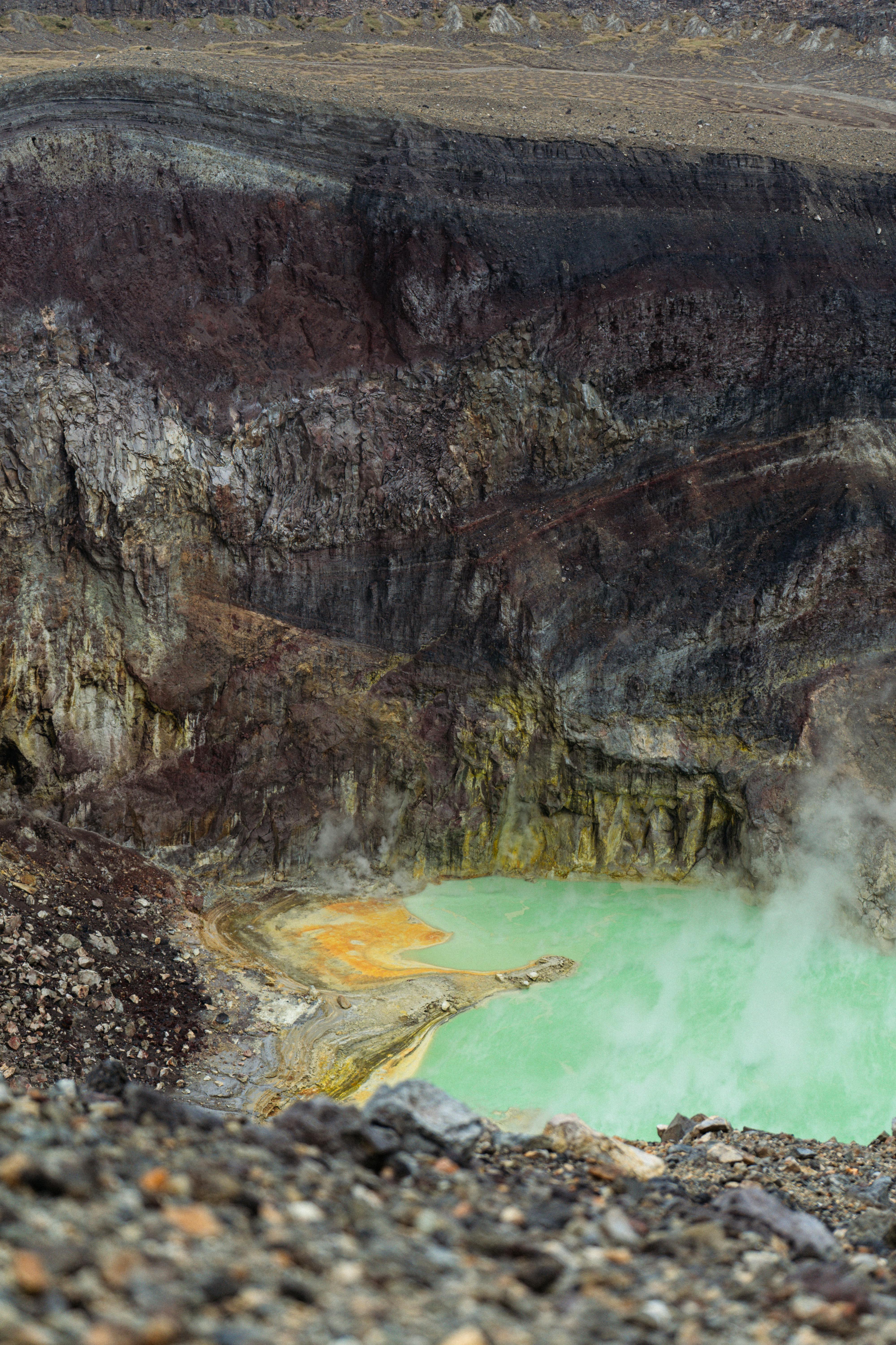Aerial shot capturing the vibrant colors of a sulfur-rich lake in a volcanic crater amidst rugged terrain.