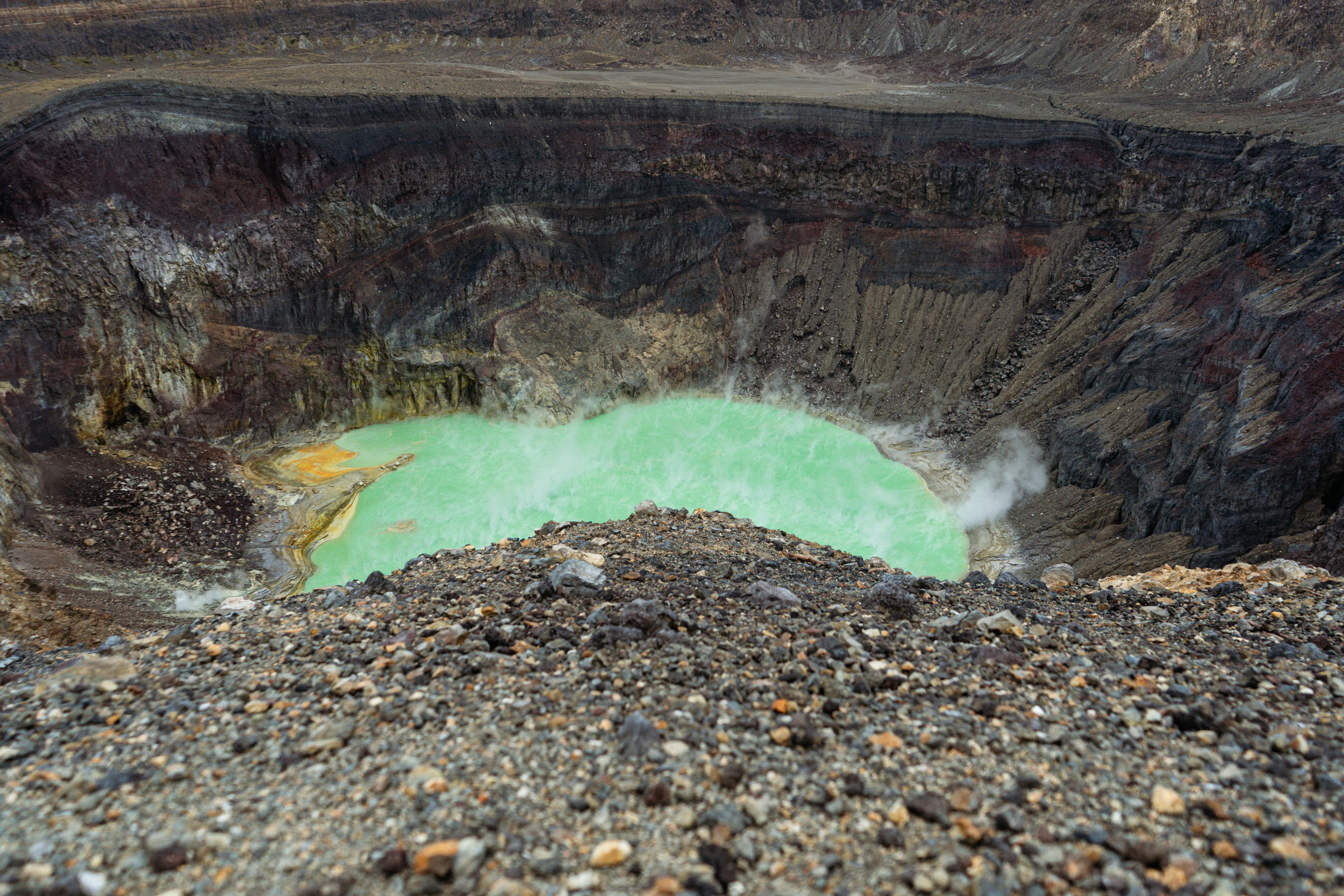 Dramatic landscape of a volcanic crater showcasing a vibrant emerald green lake surrounded by rugged terrain.
