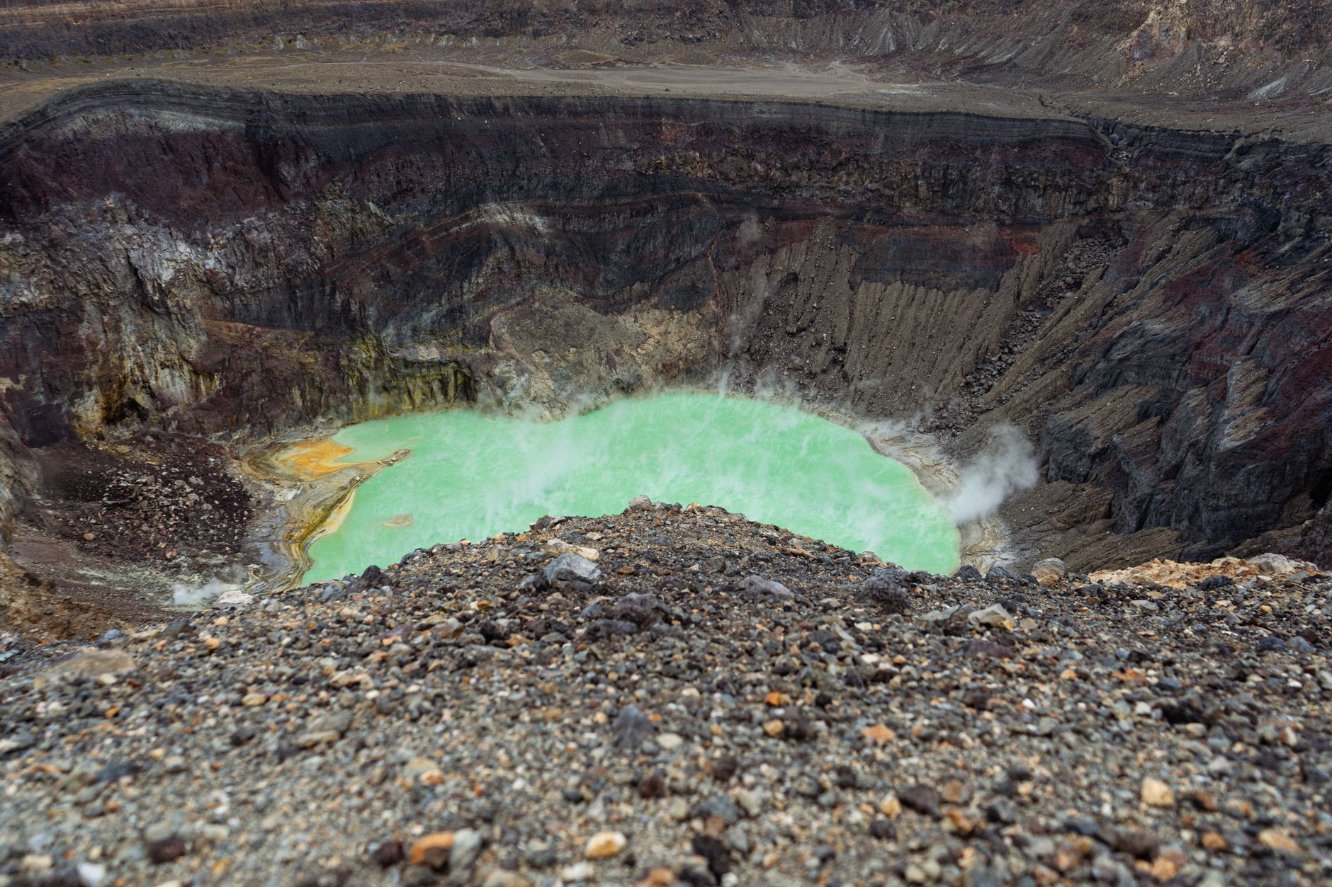 Dramatic landscape of a volcanic crater showcasing a vibrant emerald green lake surrounded by rugged terrain.