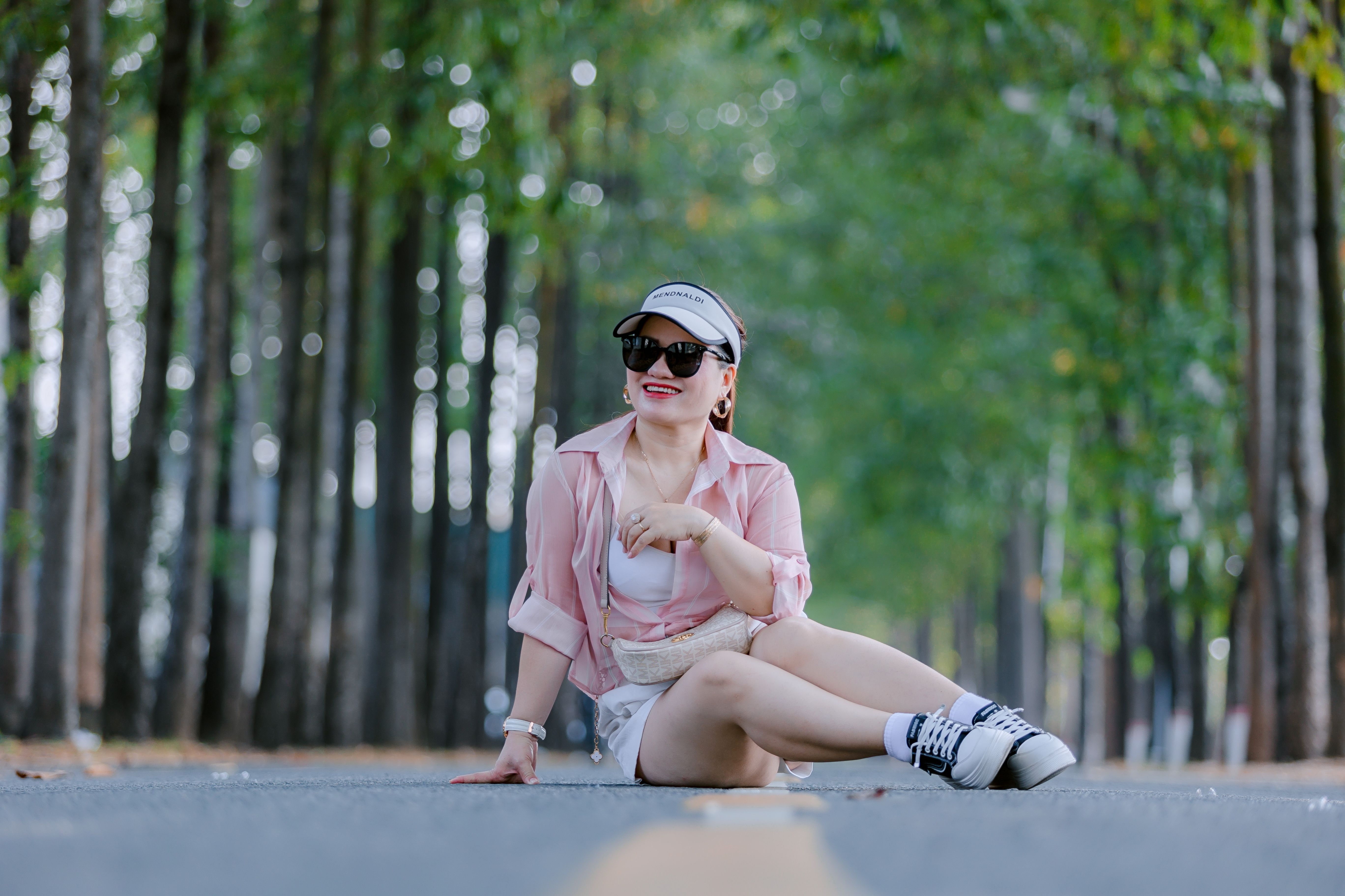 Casual woman sitting on a road surrounded by trees, enjoying a sunny day.