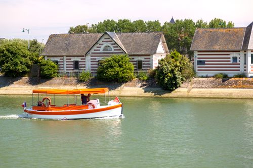 Free A colorful riverboat sails past unique striped buildings on a sunny day. Stock Photo