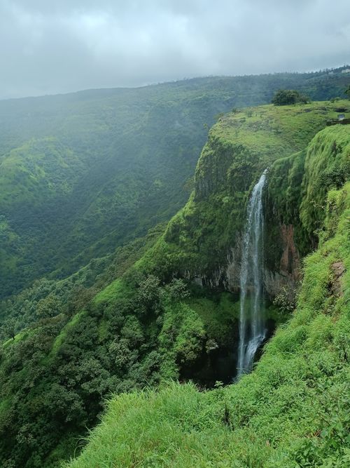Free Breathtaking view of a tall waterfall cascading down a verdant cliff in a lush green valley. Stock Photo