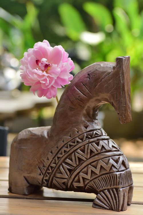 Free Artistic wooden vase with intricate carvings, holding a vibrant pink flower. Outdoors. Stock Photo