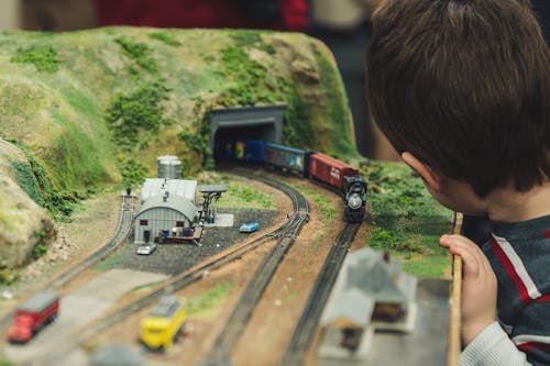 Back view of preschool boy with dark hair playing with toy train railway model while carriage passing through tunnel