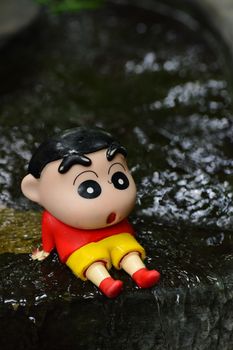 Adorable cartoon-style figurine resting on a wet stone, capturing a playful moment.