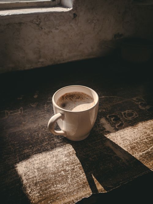 Free A cozy cup of coffee casting a shadow on a rustic table by a window. Stock Photo