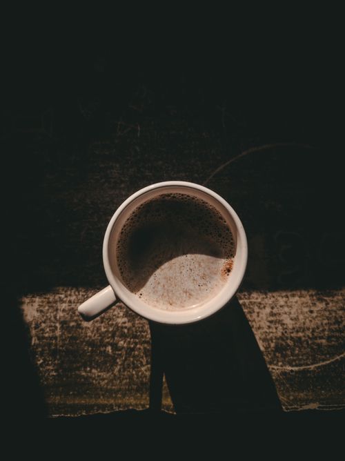 Free A warm overhead shot of coffee in a white mug casting a shadow. Stock Photo