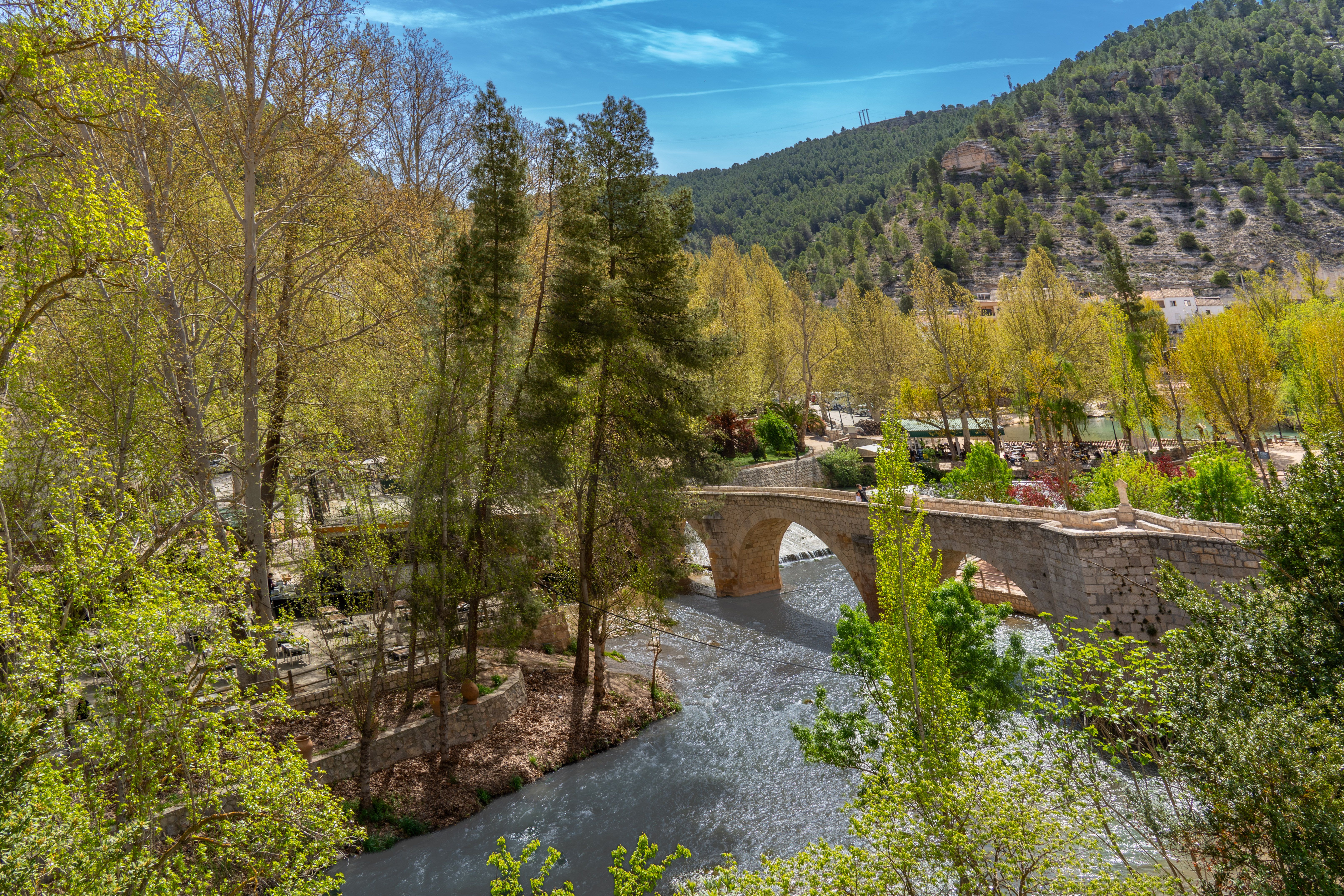 Scenic spring view of Alcalá del Júcar bridge and river surrounded by lush greenery.