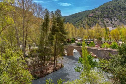 Free Scenic spring view of Alcalá del Júcar bridge and river surrounded by lush greenery. Stock Photo