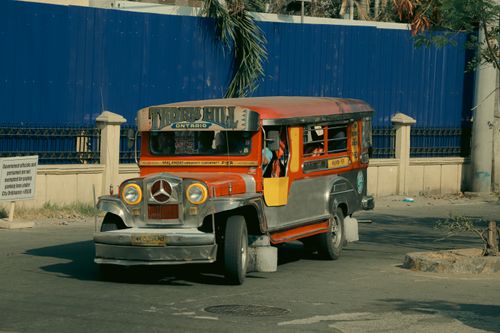 Free A vibrant jeepney travels down a city street, showcasing traditional Filipino public transport. Stock Photo