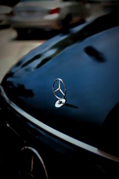 Detailed close-up of a car hood emblem reflecting on a shiny surface with blurred vehicles in the background.
