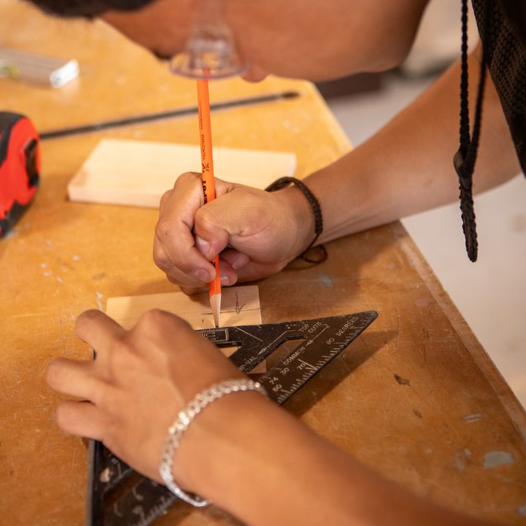 Carpenter marking precise measurements on wood with a pencil and square