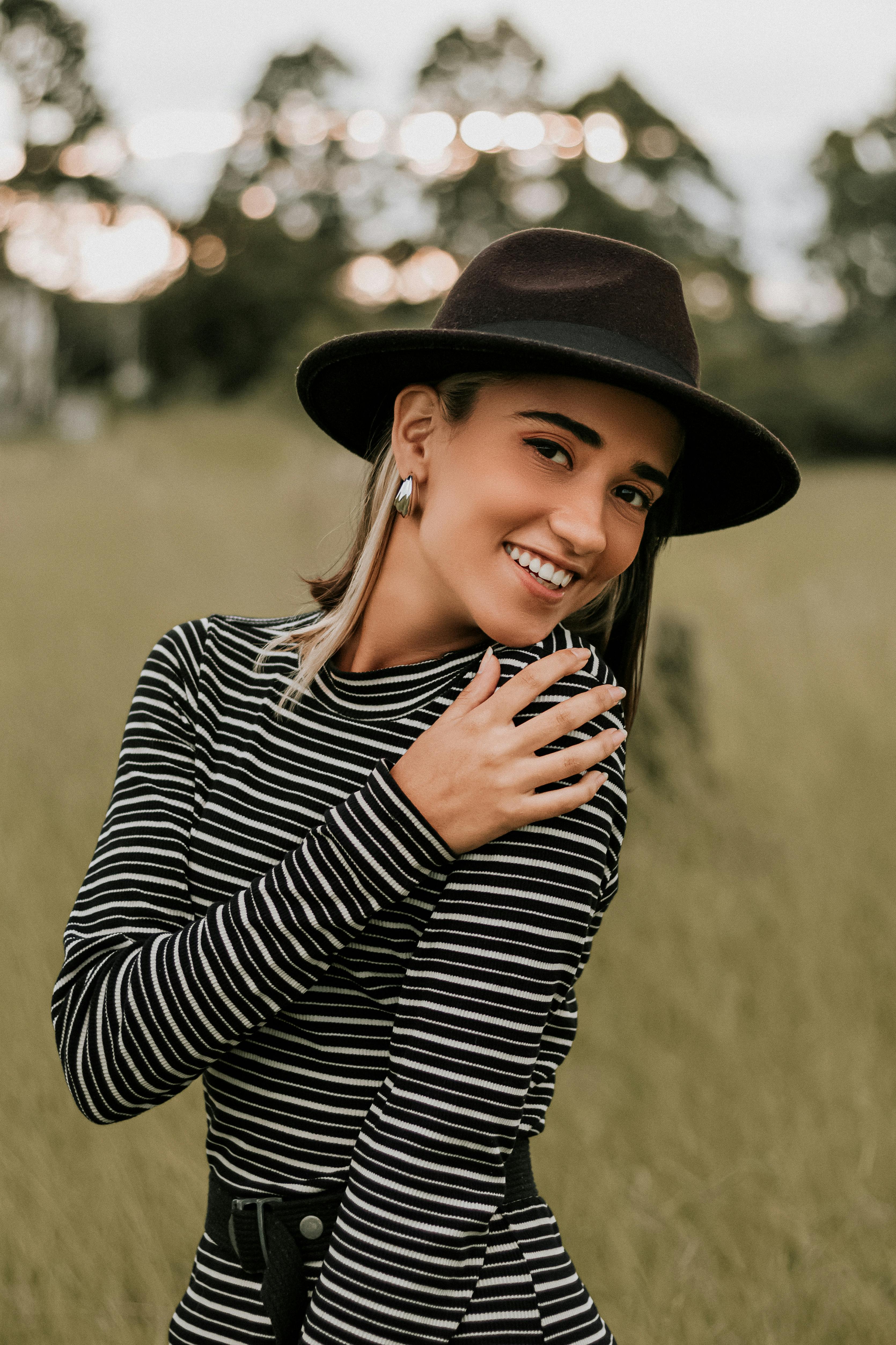 阳光明媚的田野里，一位穿着条纹连衣裙、戴着帽子的女人微笑着