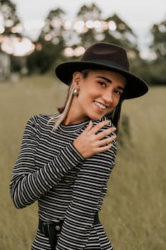 阳光明媚的田野里，一位穿着条纹连衣裙、戴着帽子的女人微笑着