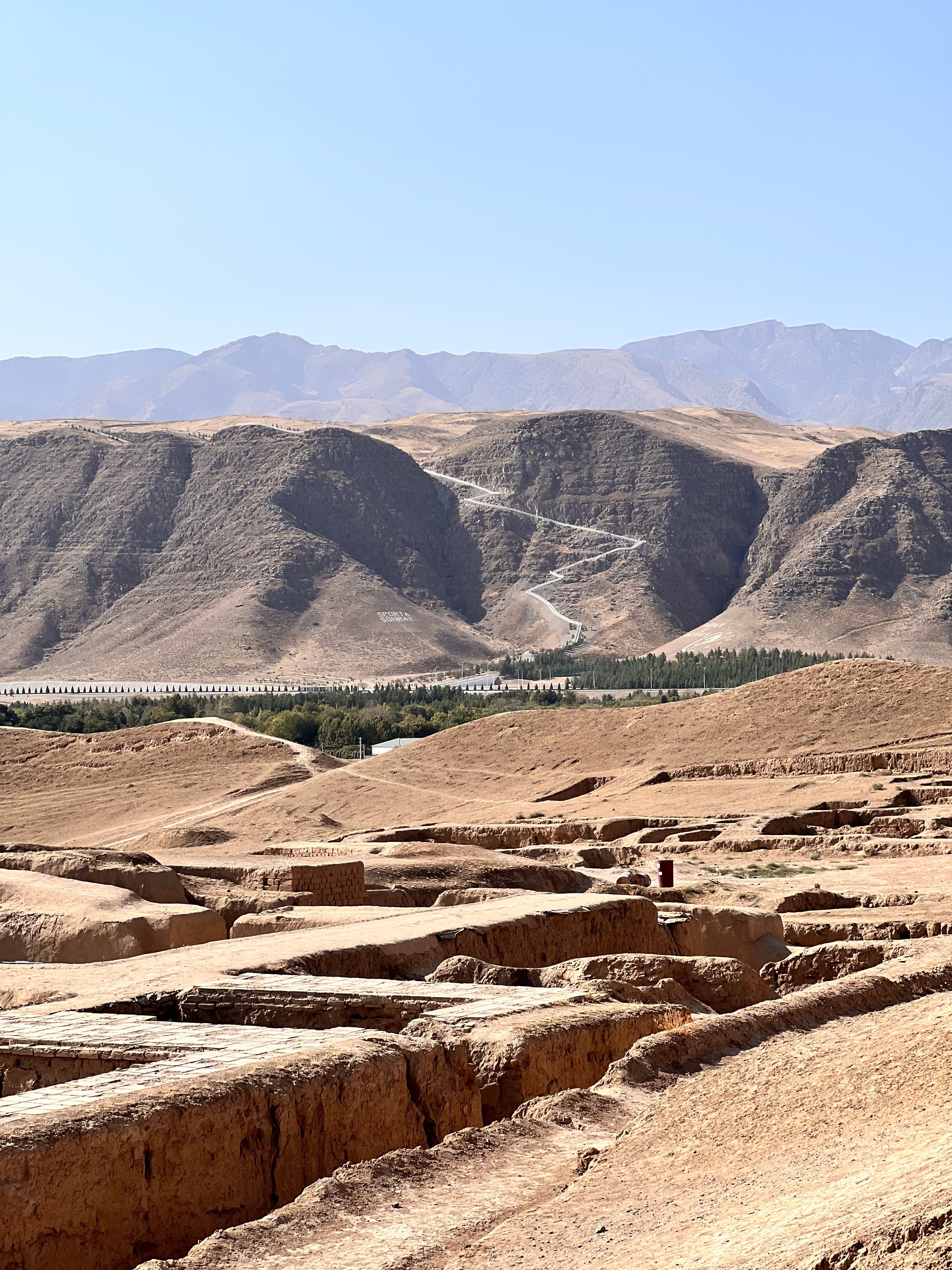 View of ancient ruins with the Karakum Desert hills in the background under a clear blue sky.