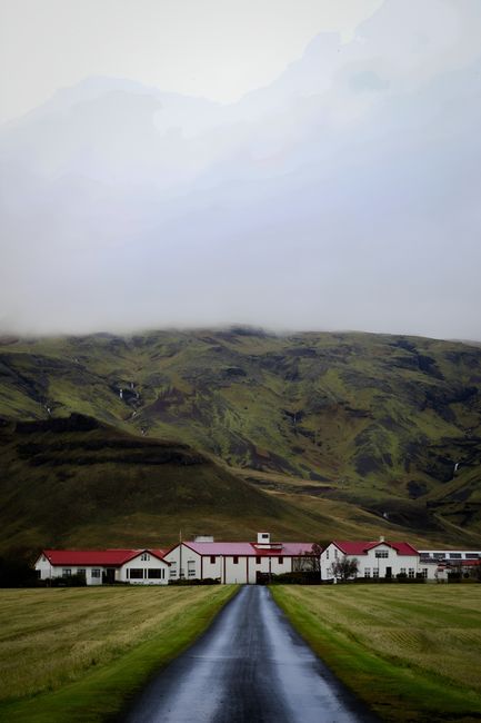 Charming house nestled against lush green mountains under a cloudy sky.