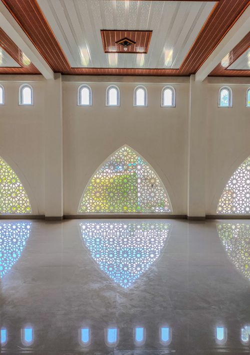 Free Bright interior of a mosque in Pacitan, Indonesia, featuring geometric window designs and reflections. Stock Photo