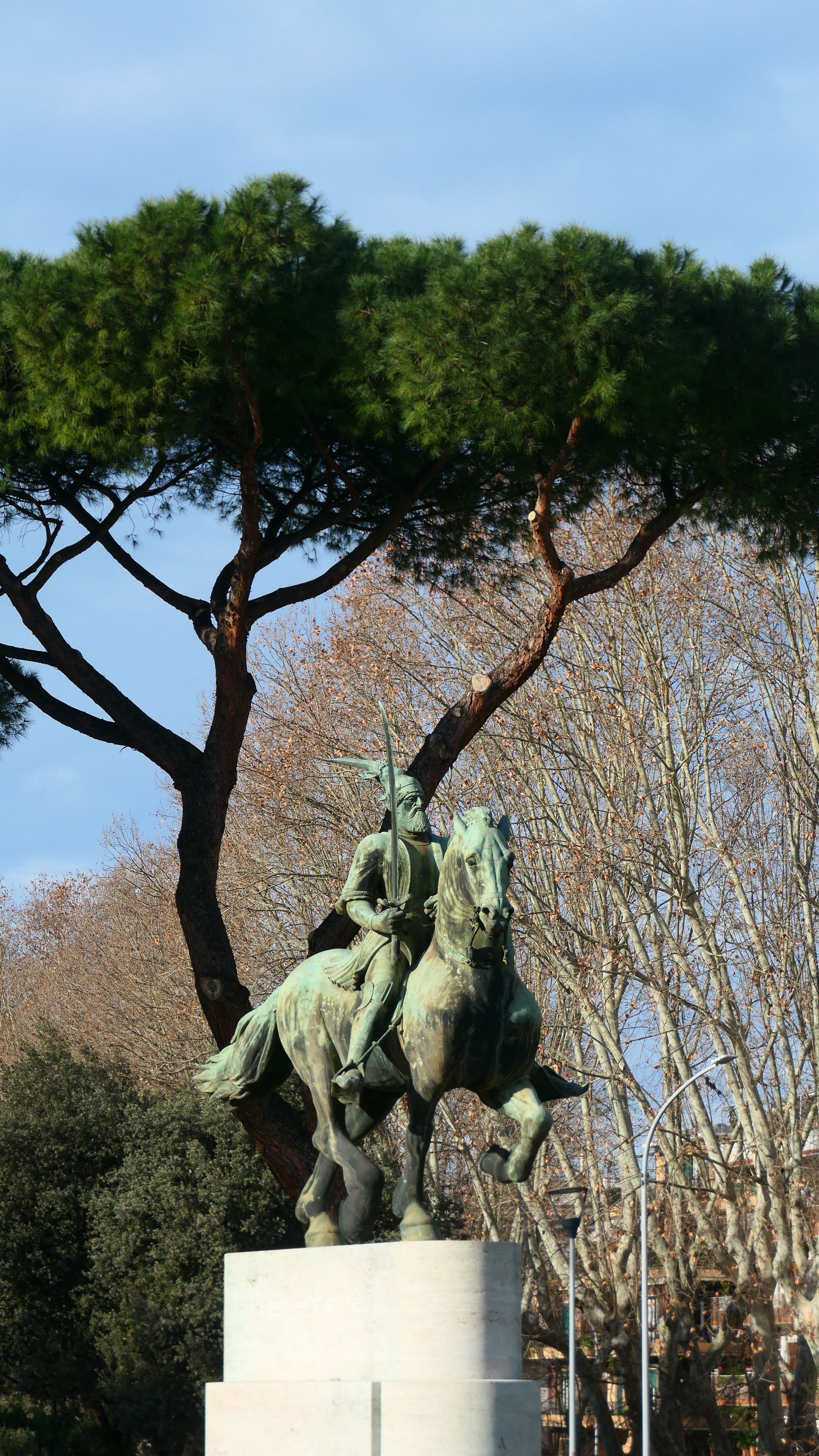 Historic bronze equestrian statue in Rome, set against lush umbrella pine trees, showcasing Italian heritage.