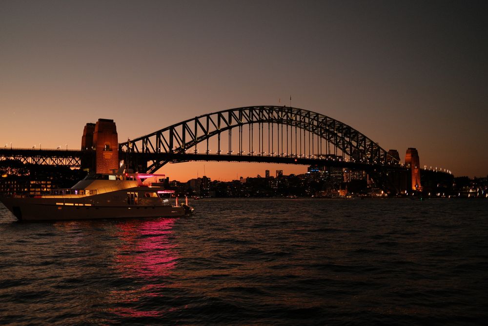 Harbour Bridge de Sydney recortado al ocaso con yate cruzando la bahía