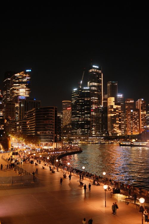 Free View of Sydney's waterfront with illuminated skyscrapers and bustling promenade at night. Stock Photo