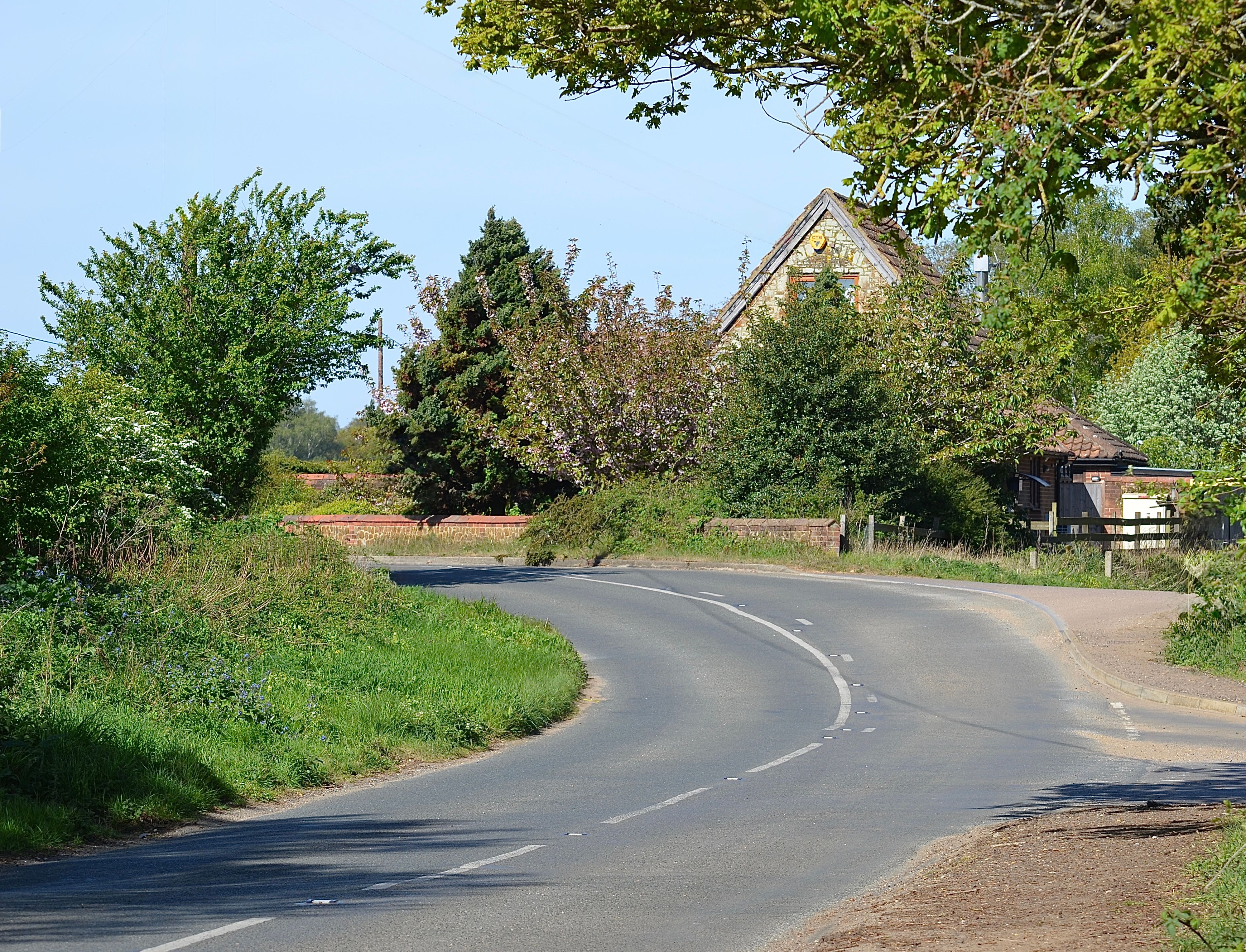 A winding country road with a rustic house and lush greenery in a serene countryside setting.