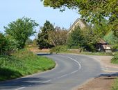 A winding country road with a rustic house and lush greenery in a serene countryside setting.