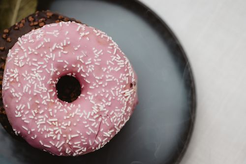 Free Top view of a pink sprinkled donut with a chocolate one beneath on a plate. Stock Photo