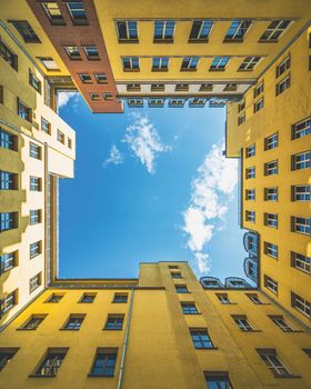 Looking up at bright yellow buildings framing a blue sky in Berlin, Germany. Urban symmetry and architectural beauty.
