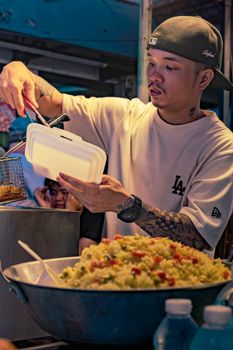 Street vendor in Manila packing fried food in a box at a bustling market stall.