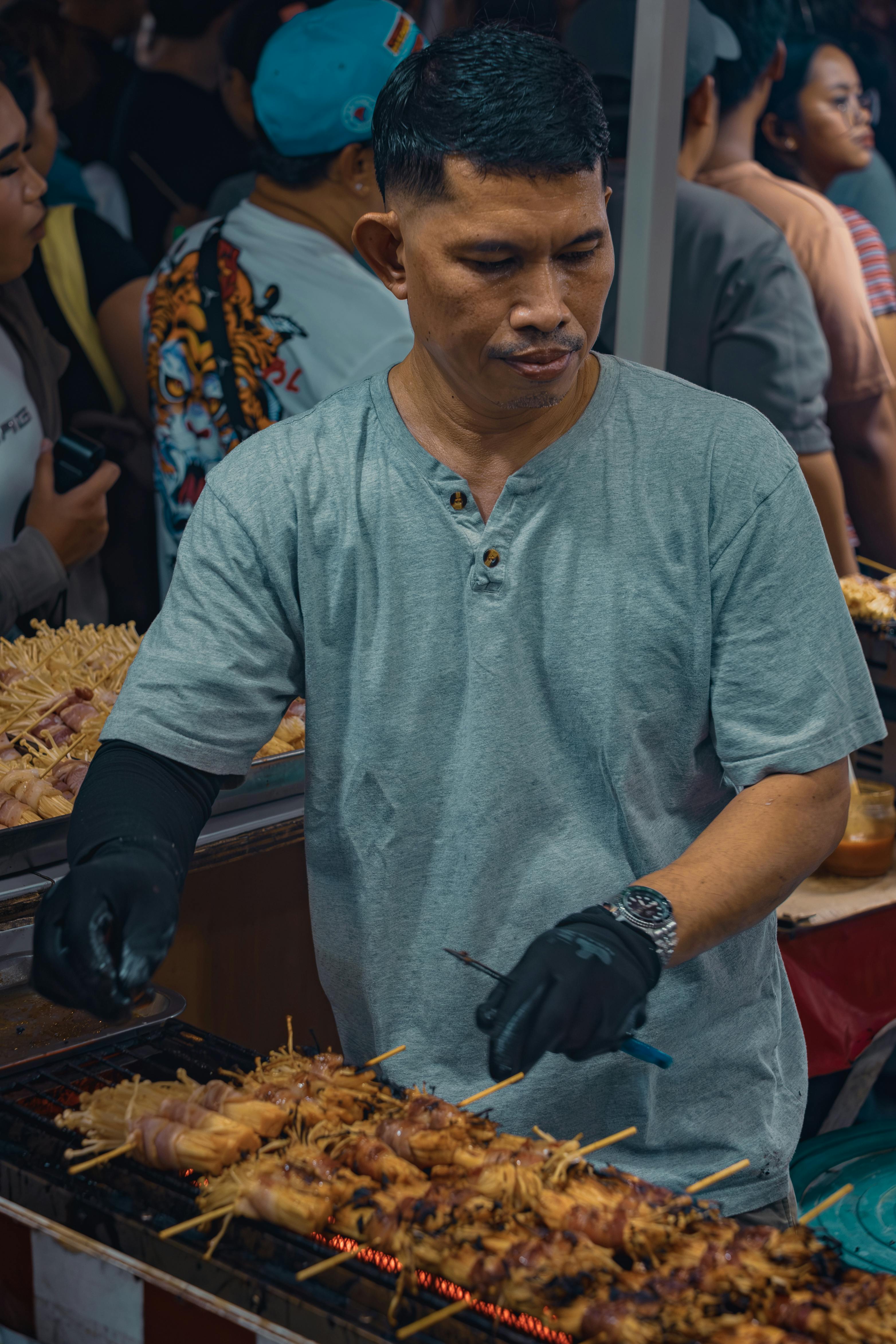 A street food vendor grills skewered meats at a bustling night market in Manila, Philippines.