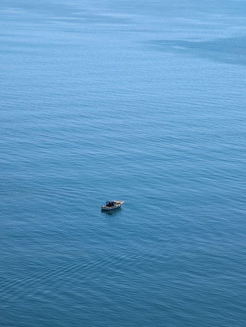 Free A lone boat drifts peacefully on the calm, expansive blue ocean, offering solitude and serenity. Stock Photo