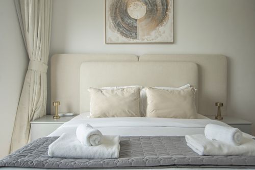Free Luxurious modern bedroom with neutral tones, plush pillows, and neatly placed towels. Stock Photo
