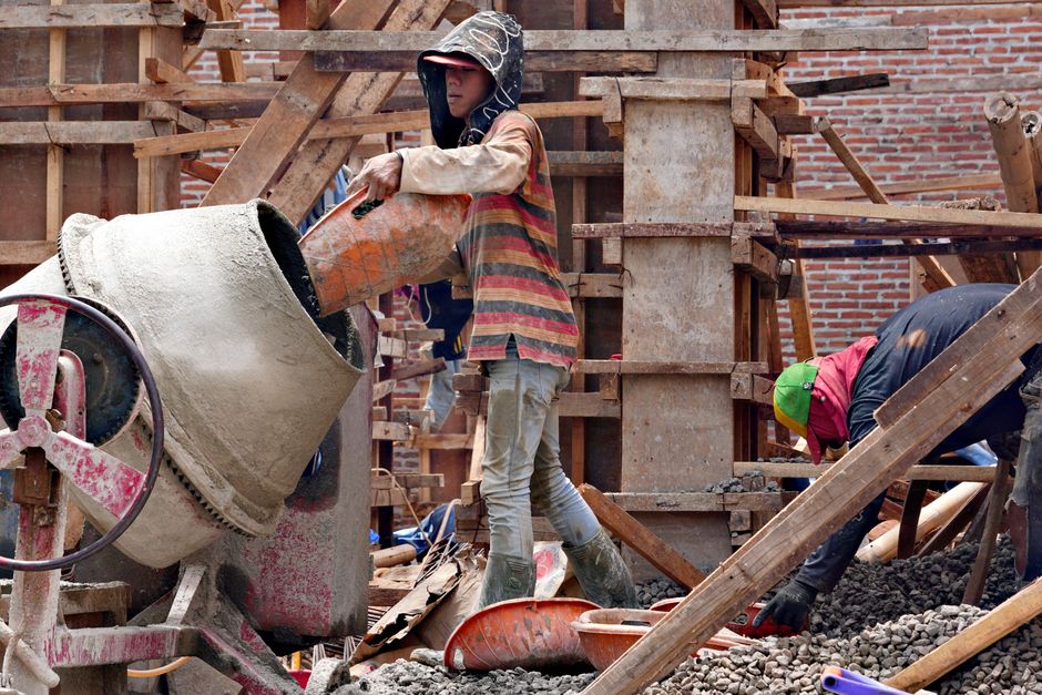 Trabajadores de construcción mezclando cemento en un sitio de obra. Trabajo manual en progreso con andamios de madera.