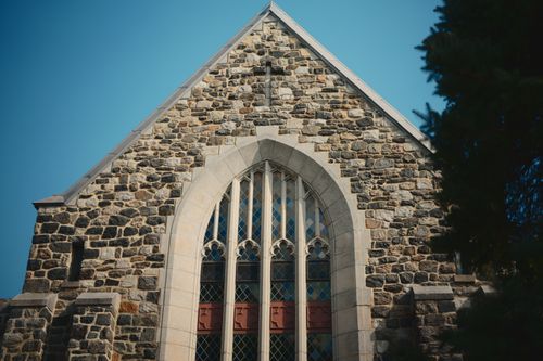 Free A beautiful stone church facade featuring a large Gothic window under clear blue skies, highlighting architectural details. Stock Photo