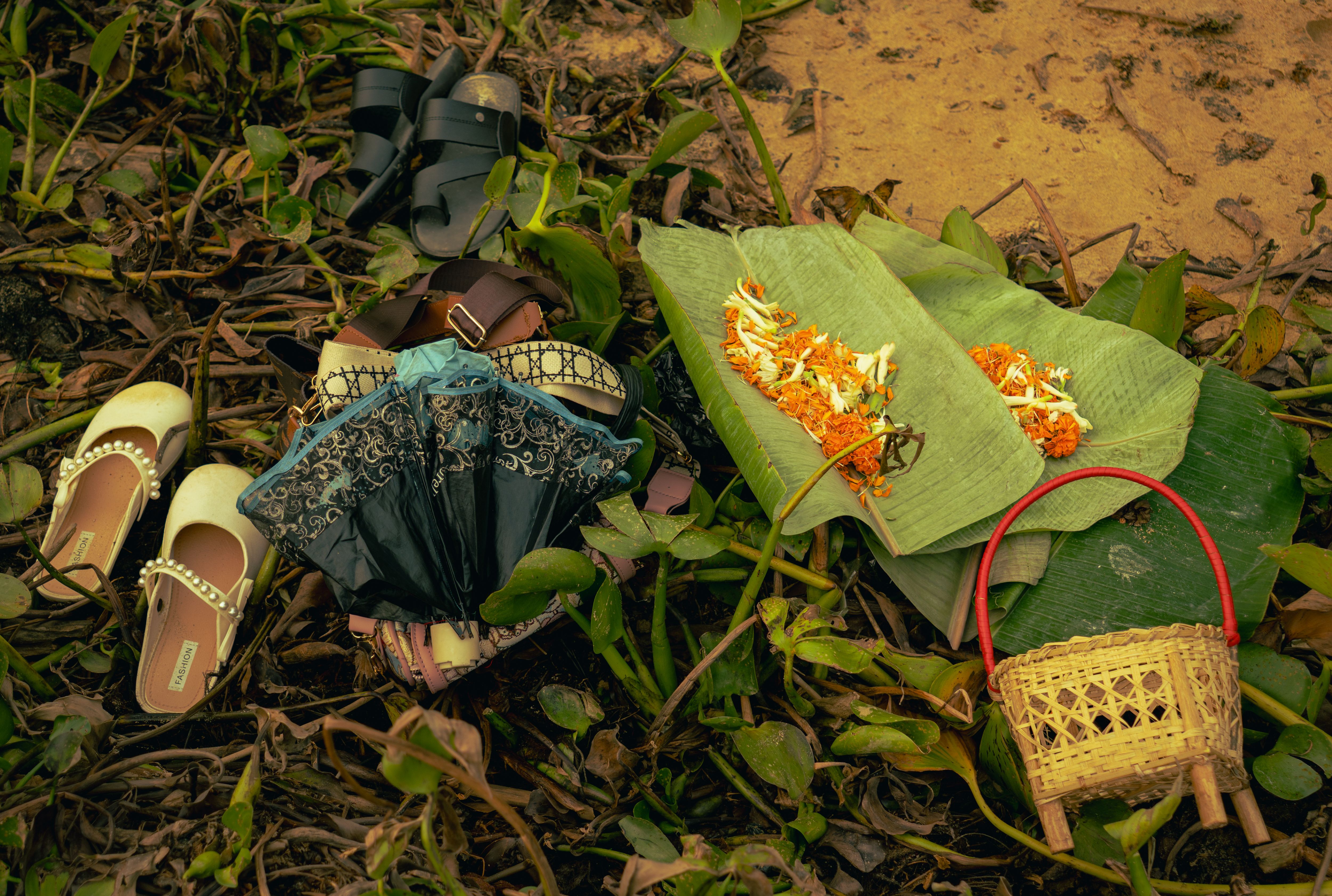 Traditional cultural offerings on banana leaves amidst nature, alongside sandals and baskets.