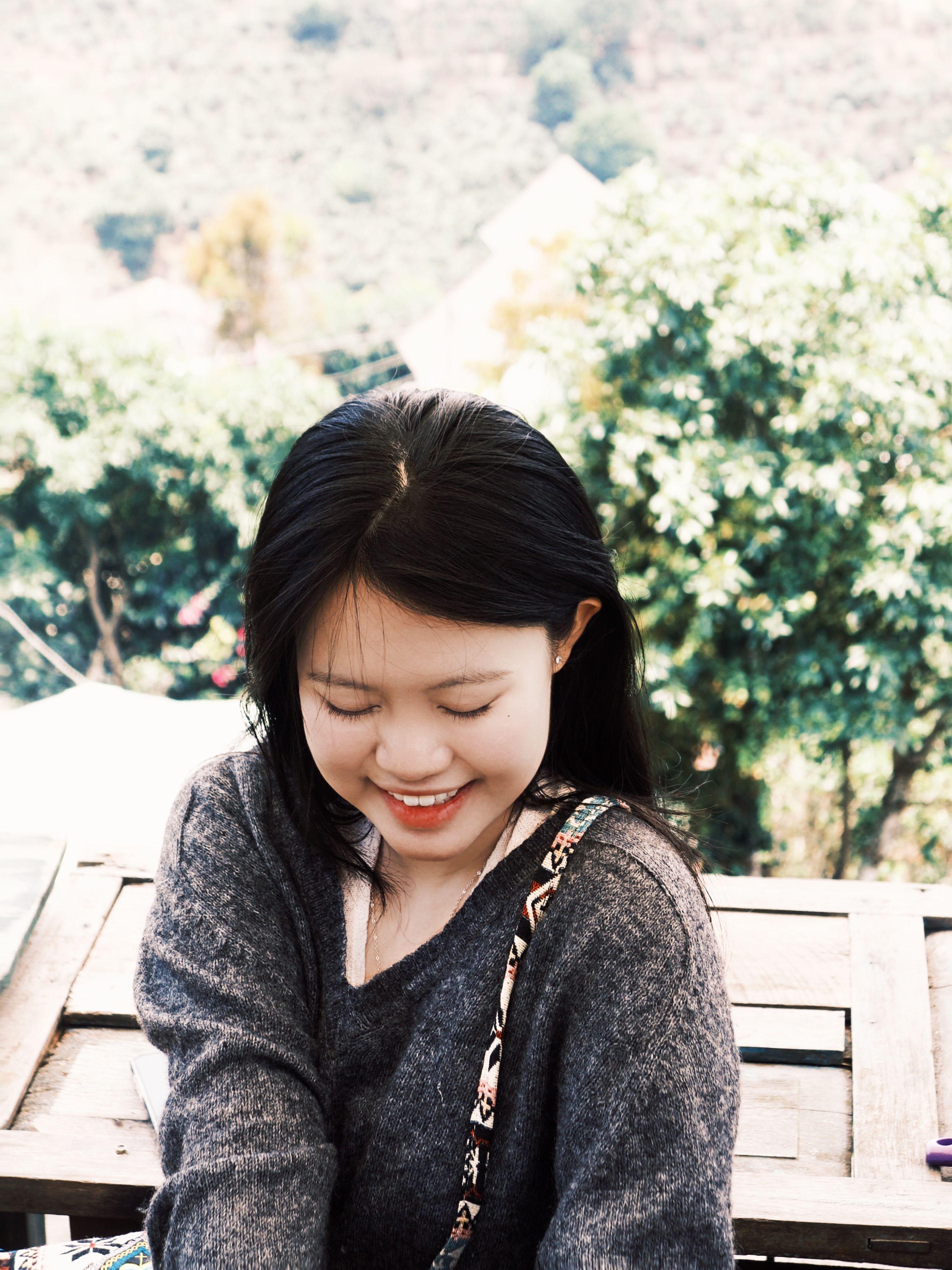 A young woman smiling peacefully outdoors in Đà Lạt, Vietnam, surrounded by lush greenery.