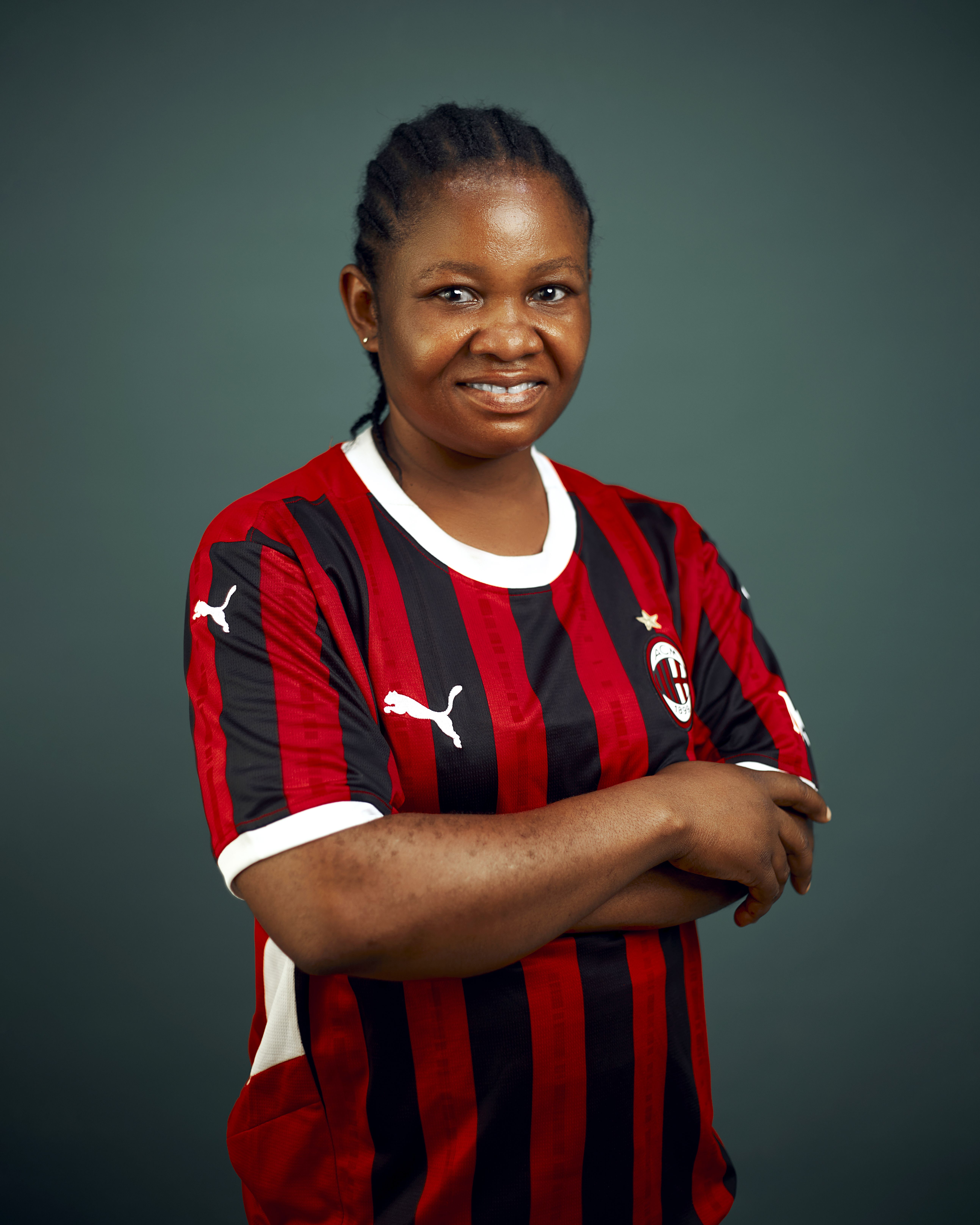 Confident woman wearing a red and black soccer jersey posing indoors with arms crossed.
