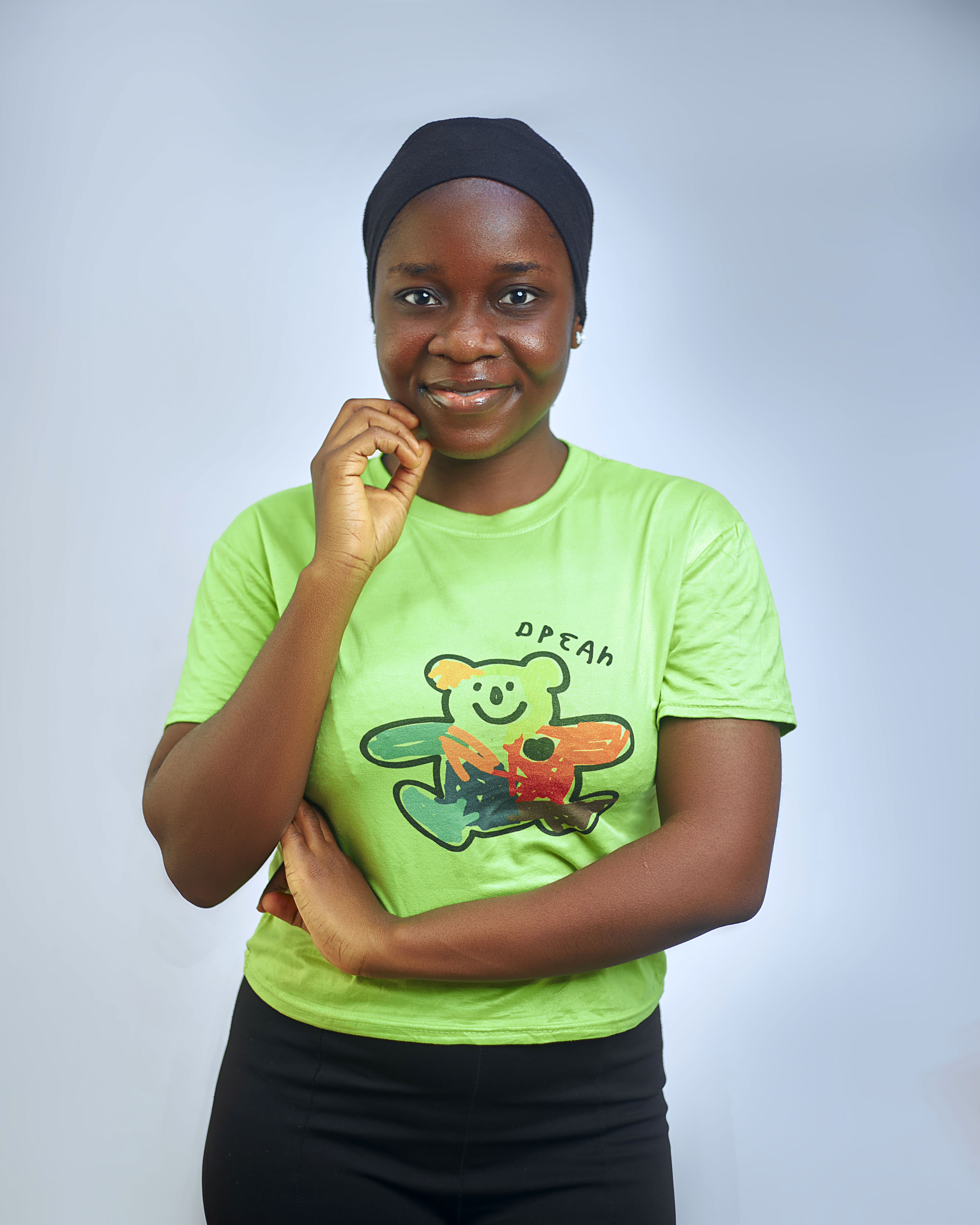 Smiling woman in green shirt, hand on chin, against white background.