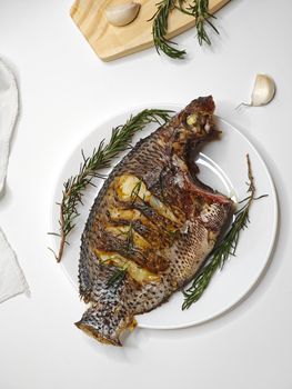 Delicious grilled tilapia garnished with fresh rosemary and garlic on a white plate.
