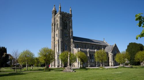 Free A majestic stone church surrounded by greenery under a clear blue sky, exemplifying Gothic architecture. Stock Photo