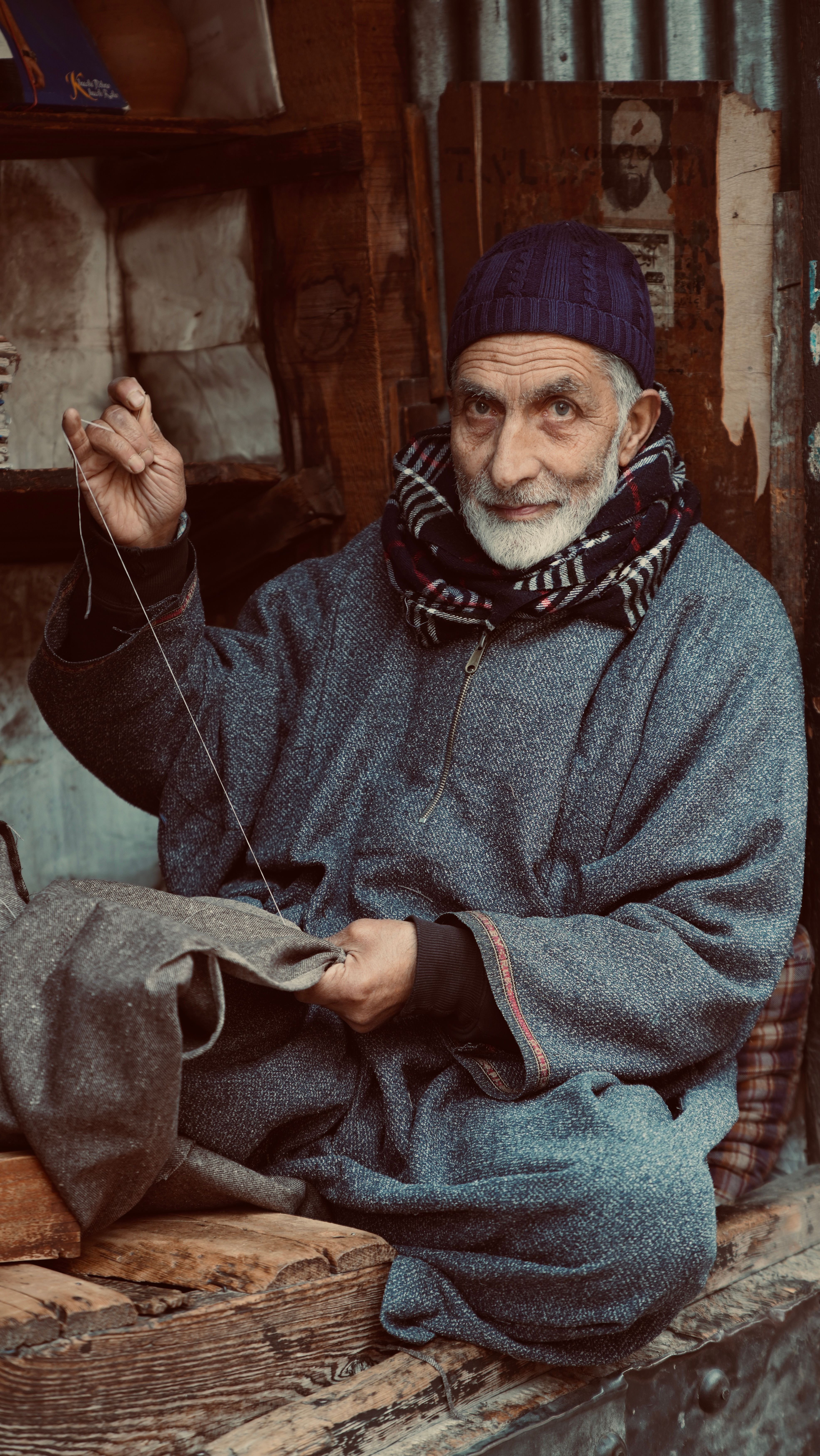 An elderly man in traditional attire sewing fabric in Srinagar, showcasing local culture and craftsmanship.