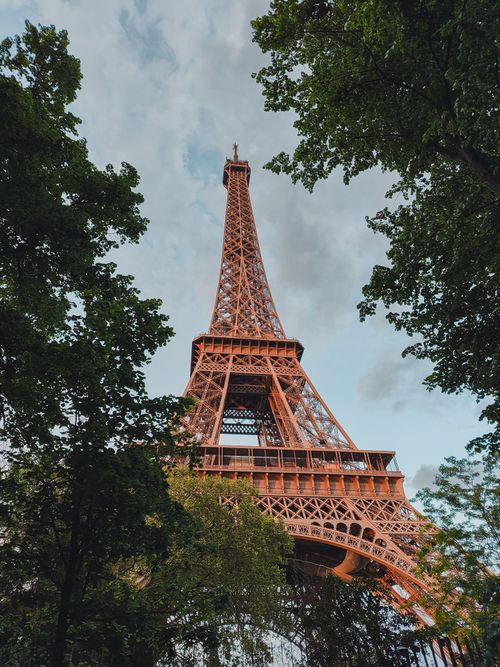 Free Scenic view of the iconic Eiffel Tower, framed by trees under a partly cloudy sky in Paris, France. Stock Photo