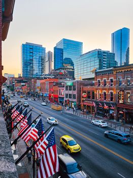 City street lined with flags and vibrant buildings under a modern skyline at sunset.