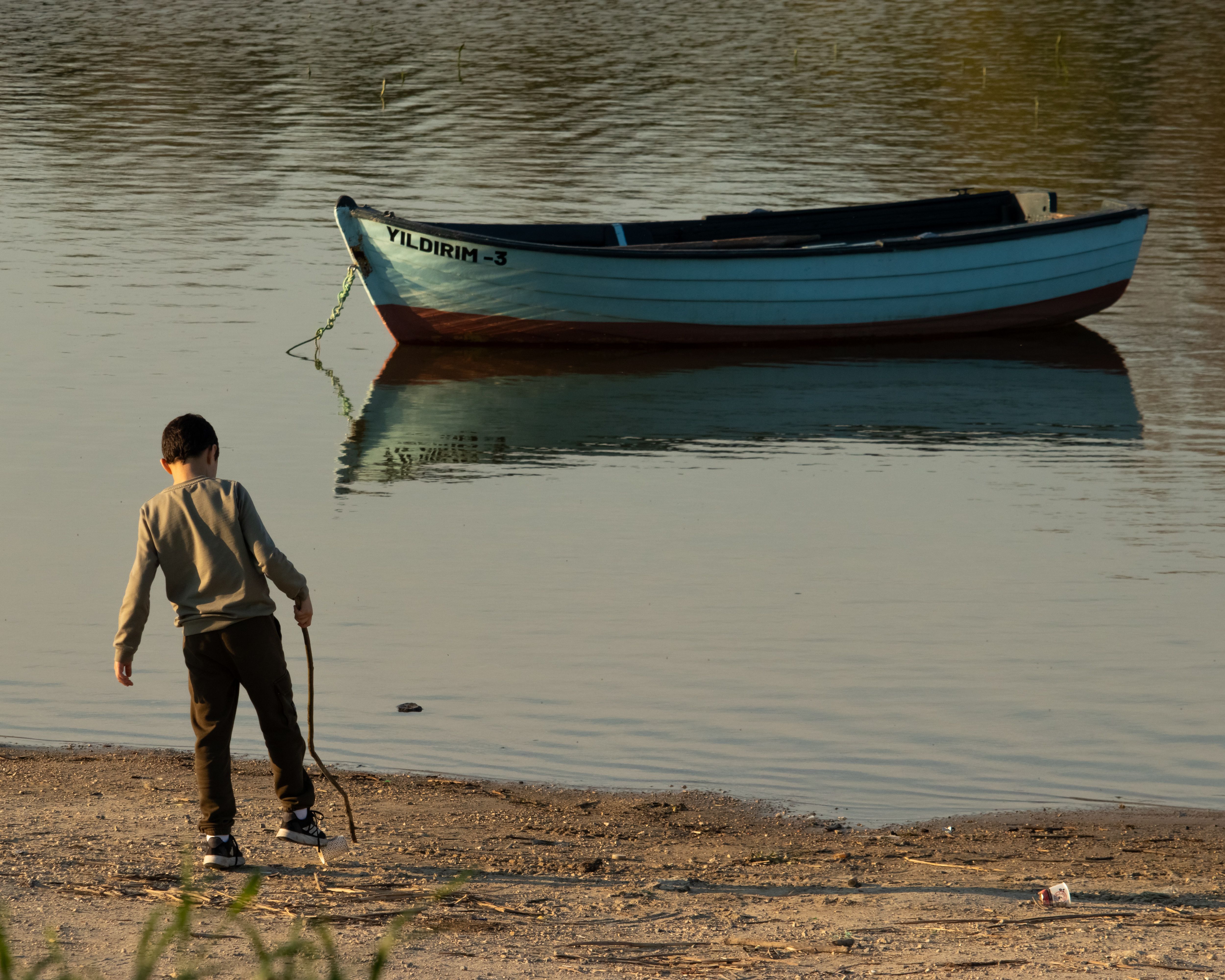 A young child plays by the lakeside near a docked boat during sunset in Arnavutköy, İstanbul.