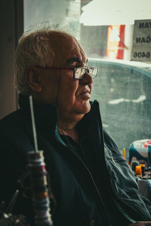 Free Elderly man in glasses sitting indoors by a window, appearing thoughtful and relaxed. Stock Photo
